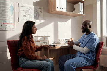 Young sick female patient and male physician discussing ways of medical treatment of disease while sitting in front of one another - obrazy, fototapety, plakaty