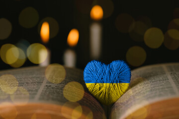 Yellow and blue heart and bible on a table by candlelight. Pray for Ukraine in the colors of the...