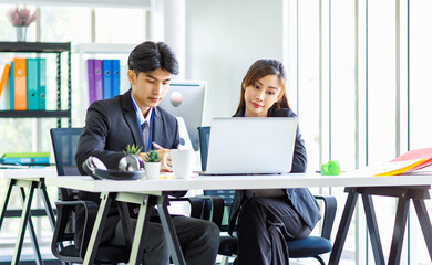 Asian young happy professional male businessman mentor and female businesswoman colleague in formal suit working discussing meeting together at workplace desk with laptop notebook computer in office