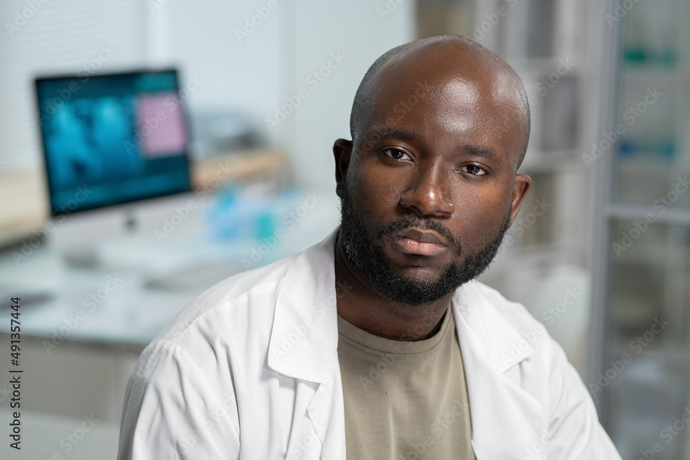 Poster Portrait of serious bearded scientist or chemist in lab coat sitting in front of camera during scientific experiment in laboratory