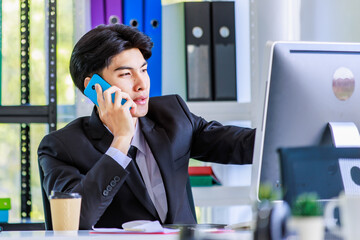 Closeup shot of Asian young worried stressed depressed upset unhappy frowning face male businessman employee staff in formal suit sitting at working desk on call chatting with customer via smartphone