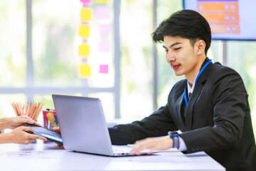 Asian young handsome professional success male businessman employee staff in formal suit sitting working with laptop notebook computer and paperwork graph chart growth target document in meeting room