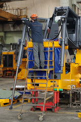 Young repairman or technician standing on stepladder by industrial machine while checking condition of working parts