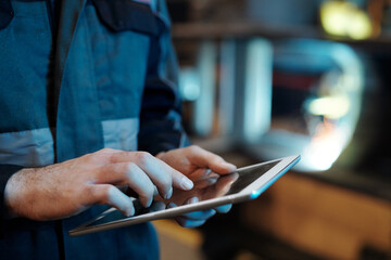 Hands of contemporary engineer of industrial plant with tablet pointing at screen or scrolling...