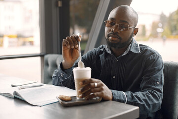 Black man sitting in a cafe with a cup of latte and papers
