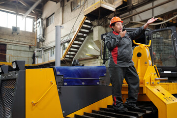 Young contemporary technician of industrial plant speaking in walkie talkie while giving...