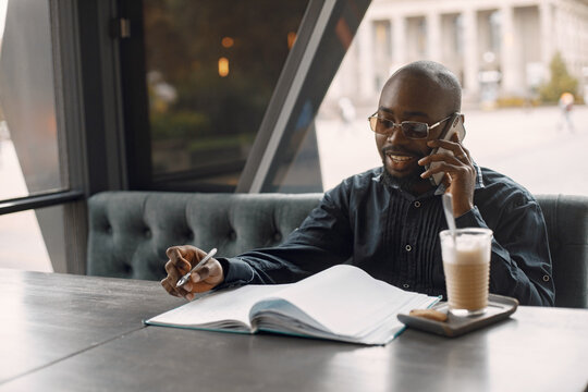 Black man sitting in a cafe with a cup of latte and using a phone