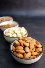 Various varieties of nuts and dried fruits are in a bowls on black background. Top view. Healthy food. Vegetarian nutrition. cashew, almond, pistachio, and raisins. Assorted nuts banner. Copy space