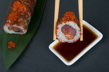 close-up, sliced rolls with caviar, fish, vegetables, tuna, as a background, on a green bamboo leaf, sticks dipped in soy sauce