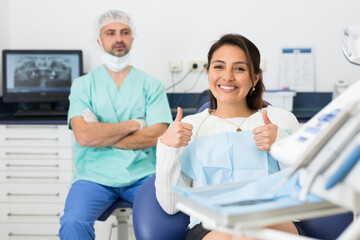 Portrait of smiling satisfied american woman visiting dentist giving thumbs up