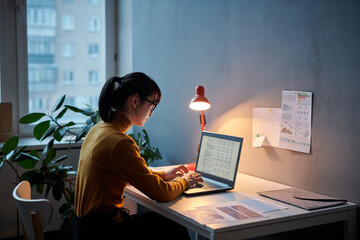 Young businesswoman sitting at her workplace and working with project online using laptop, she...