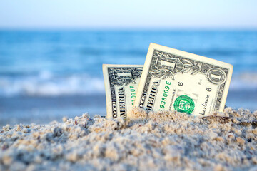 Two one dollar bills half buried in sand on sandy seashore close-up. Two paper dollar bills half in...