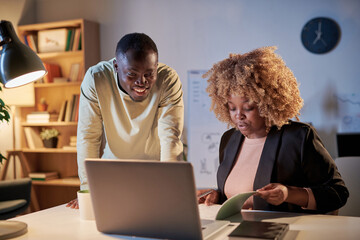 African woman examining the project sitting at table in front of laptop and discussing it with her...