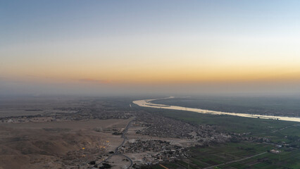 Aerial view of the Nile Valley in Luxor. You can see the deserted archaeological zone, green fields, bends of the river. The dawn sky is highlighted in orange. Egypt