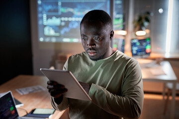 African programmer examining the new software on digital tablet, he working at office till late evening