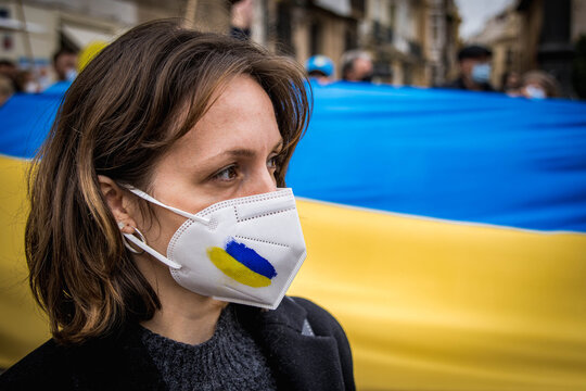 Close-up of Ukrainian Woman with Mask Painted Blue and White and the National Flag in the Background in Protest against the War