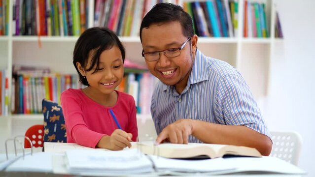 Happy little girl studying with teacher in library