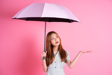 Young Asian woman holding umbrella on pink background