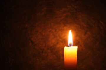 Fototapeta na wymiar Burning candle against a dark concrete wall.