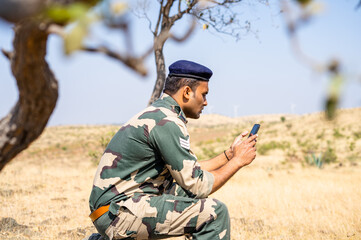 Young indian soldier uniform using mobile phone on top of mountian - concept of technology, relaxation and distant internet connection or service.