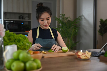 Healthy young woman sitting at kitchen counter and cutting fresh organic apple on wooden board.