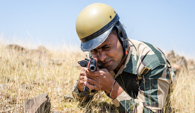 Army solider with gun aiming for target while hinding behinf the rock stones on hill top - concet of war fare tactics, combat and surveillance