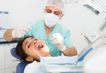 Fototapeta premium Dentist man examining a latin female patient teeth with dental tools - mirror and probe