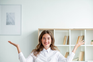 Finish work. Happy woman. Enjoying moment. Elegant pretty smiling lady in white shirt sitting desk hands up in light room interior copy space.