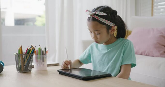 Asia young student Alpha gen Z girl fun play look at touch screen use stylus pen design idea coloring art on home school online class app. Smart kid happy leisure indoor activity sit at table sofa.