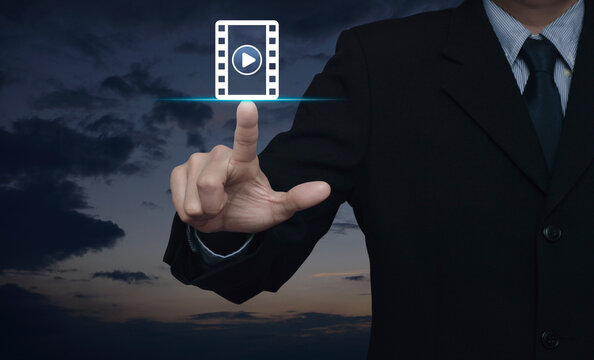 Businessman pressing play button with movie flat icon over sunset sky, Business cinema online concept