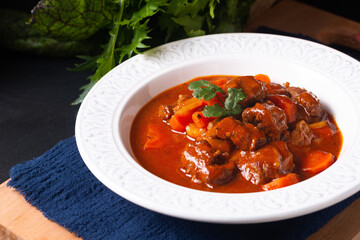 Food concept Homemade French Stew Beef Marengo in white ceramic soup plate on wooden board on black slate stone background with copy space