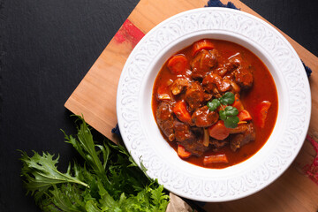 Food concept Homemade French Stew Beef Marengo in white ceramic soup plate on wooden board on black slate stone background with copy space