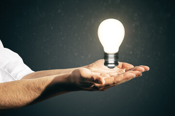 Close up of businessman palms holding glowing light bulb. Idea and innovation concept.