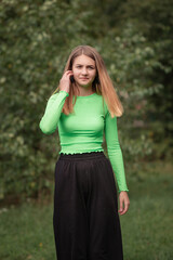 Portrait of a young beautiful girl in a green blouse in the park in summer.