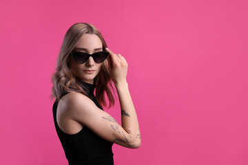 Beautiful woman with tattoos on arm against pink background. Space for text