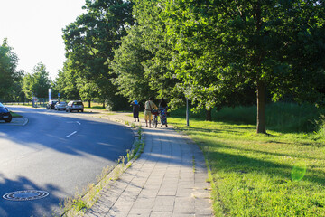 View of park and empty road with people on sidewalk in Itzehoe, Germany with bright sunny sky background.