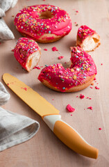 round donuts with pink icing on a wooden board, a knife and a cotton napkin lie nearby. Bright arrangement of sweets