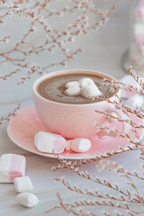 Coffee in a pink rimmed cup surrounded by white flowers and marshmallows on a light background. Delicate breakfast in a stylish interior