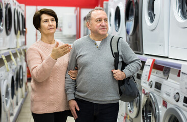 Fototapeta na wymiar Happy spouses of mature age, who came to the electronics and household appliances store for shopping, choose a washing .machine