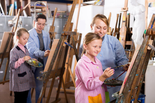 Positive female teacher helping girl during painting class at art studio