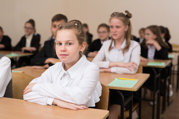 Happy schoolchildren sit at a desk in the classroom