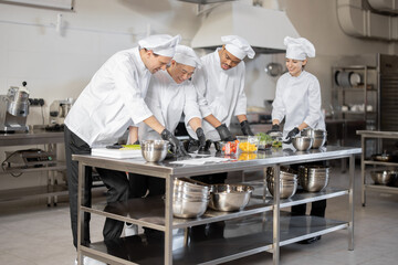 Fototapeta na wymiar Multiracial team of cooks mixing ingredients for take away food in professional kitchen. Concept of dark kitchen for cooking for delivery. Idea of teamwork in a restaurant. Diverse people at job