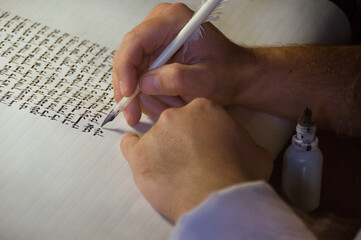 Closeup view of the hands of a Jewish scribe writing the Hebrew text of the Torah or Bible on...