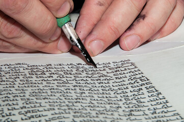 Closeup view of the hands of a Jewish scribe writing the Hebrew text of the Torah or Bible on...