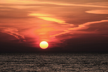 sun setting in the sea with cloud trails