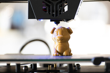 Detail of a 3D printer printing a model with a gold biodegradable PLA filament, ecofil, blue light