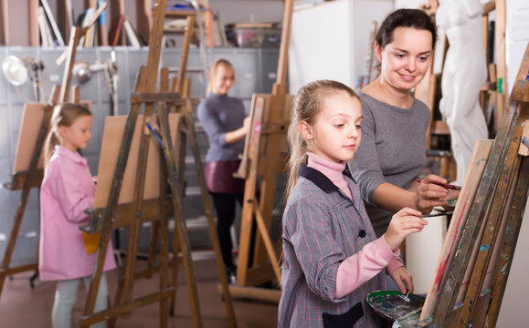 Female teacher assisting girl during painting class at art studio