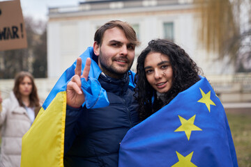 Man and woman covered with EU and Ukraine flags and showing peace sign