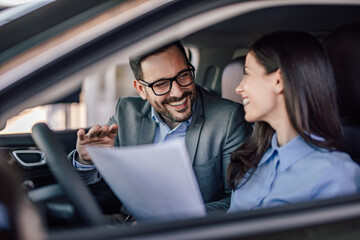 Smiling adult people, looking at the contract about the car purc