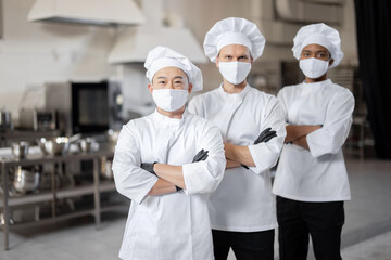 Portrait of multiracial team of three chefs standing together in the professional kitchen....